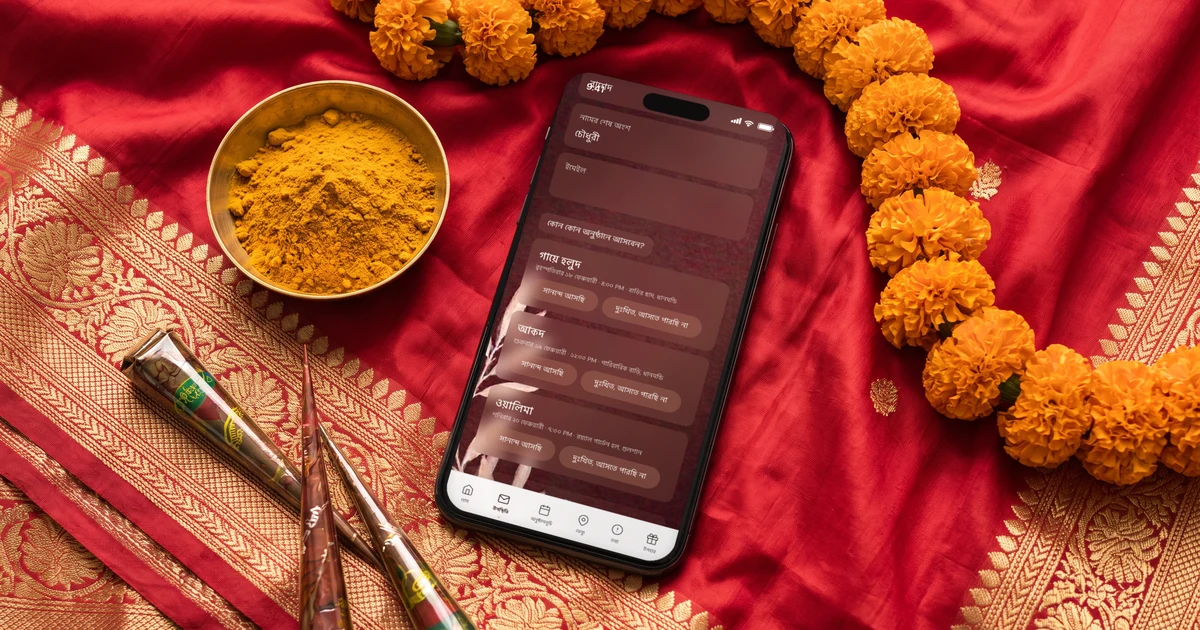 লাল-সোনালি বেনারসি শাড়ির ওপর রাখা ফোনে ডিজিটাল বিয়ের দাওয়াত কার্ড, পাশে কাঁচা হলুদ, মেহেদি আর গাঁদা ফুলের মালা: RSVP সহ বিয়ের কার্ড অ্যাপ
