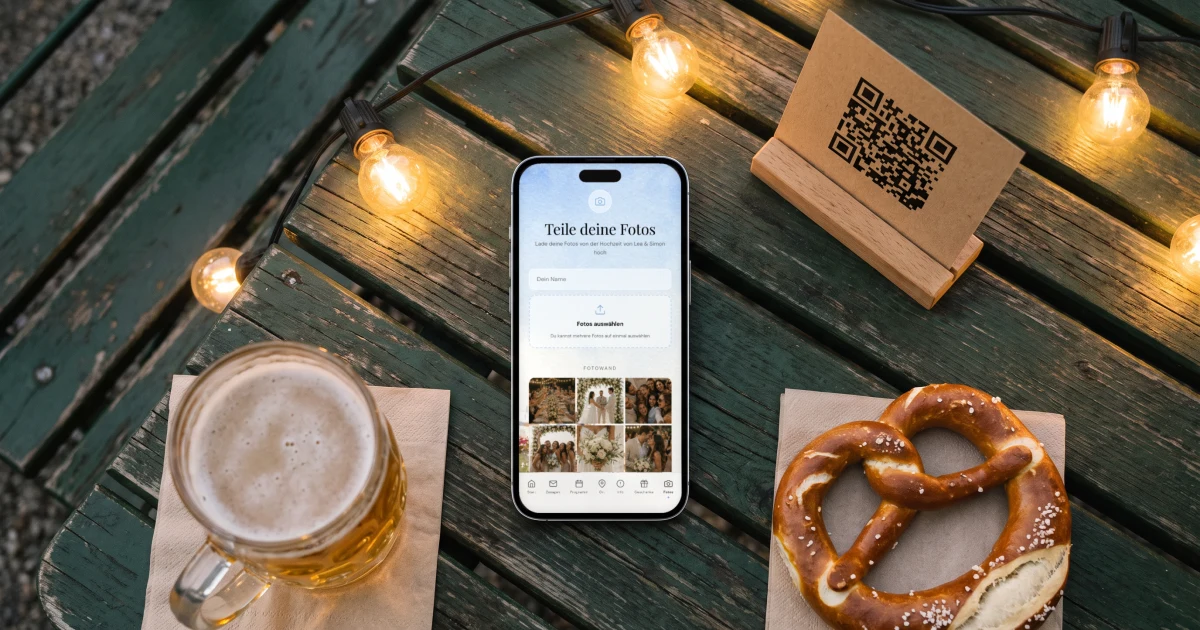 App für Hochzeitsfotos der Gäste: ein Handy zeigt die Fotowand neben einer QR-Karte, einer Brezel und einem Bier im Biergarten
