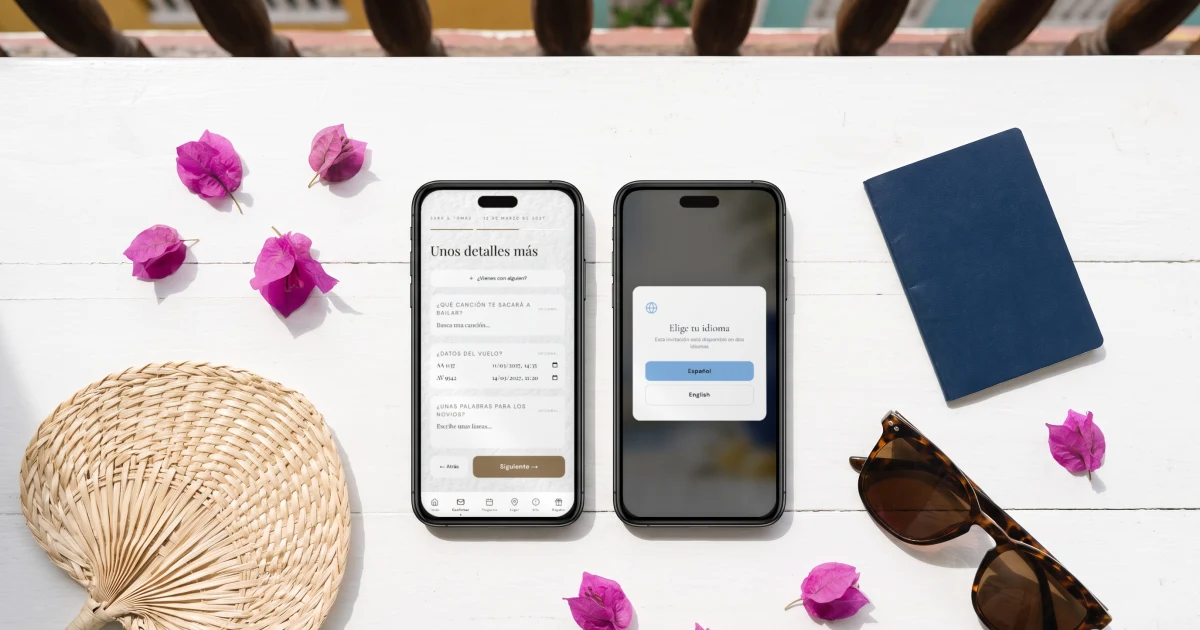 Boda en Cartagena: dos celulares sobre una mesa blanca con buganvilias muestran la confirmación de asistencia con el vuelo de llegada del invitado y el selector de idioma español e inglés de la invitación, junto a un pasaporte, gafas de sol y un abanico de palma