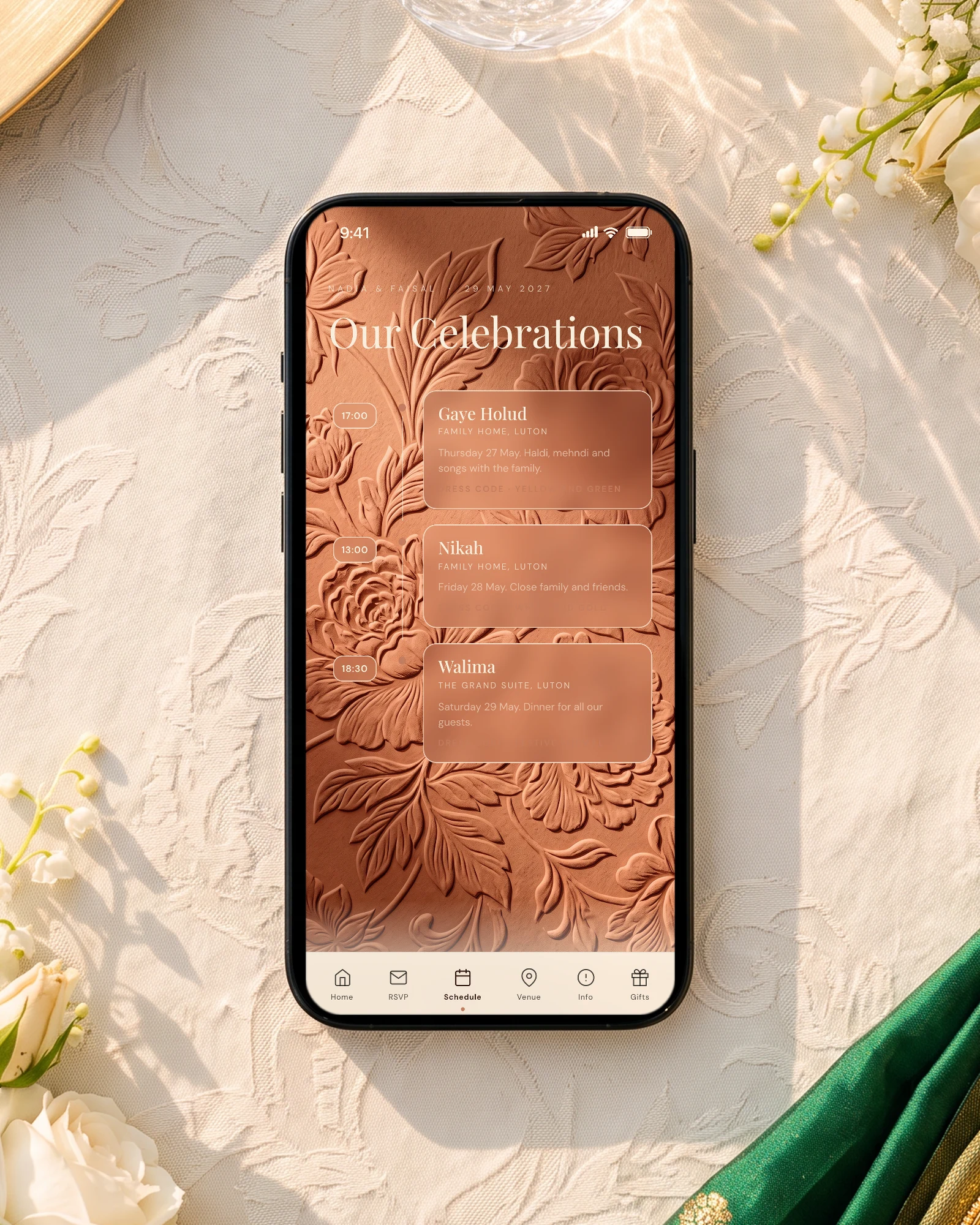 British-Bangladeshi wedding schedule on a phone lying on an ivory walima table with white roses, a gold charger and an emerald silk dupatta: the invitation shows Gaye Holud, Nikah and Walima with their times and Luton venues