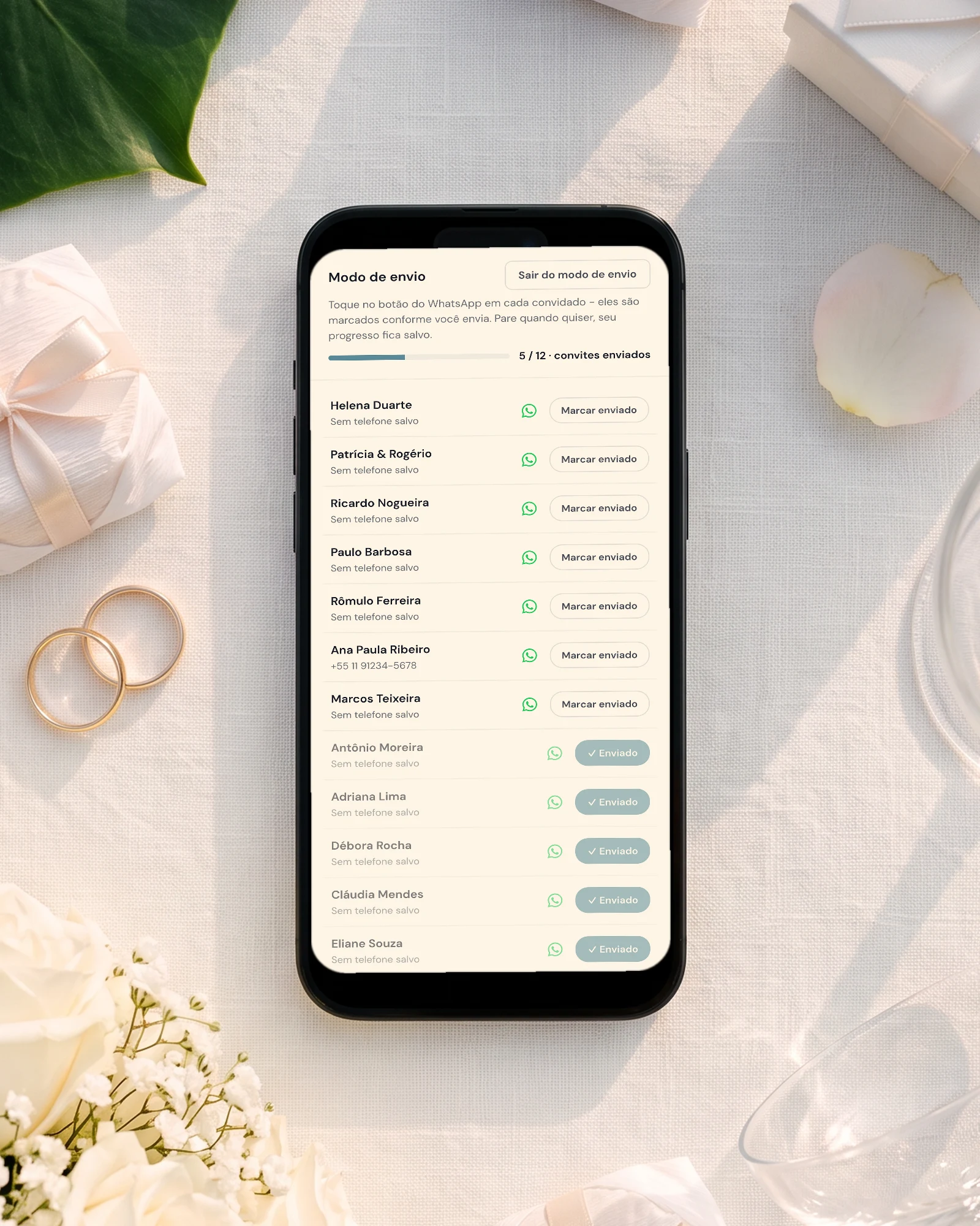 Convite de casamento pelo WhatsApp: o celular mostra o modo de envio com o botão de WhatsApp de cada convidado e a barra de progresso dos convites enviados, entre bem-casados, alianças, uma caixinha para padrinhos e flores brancas