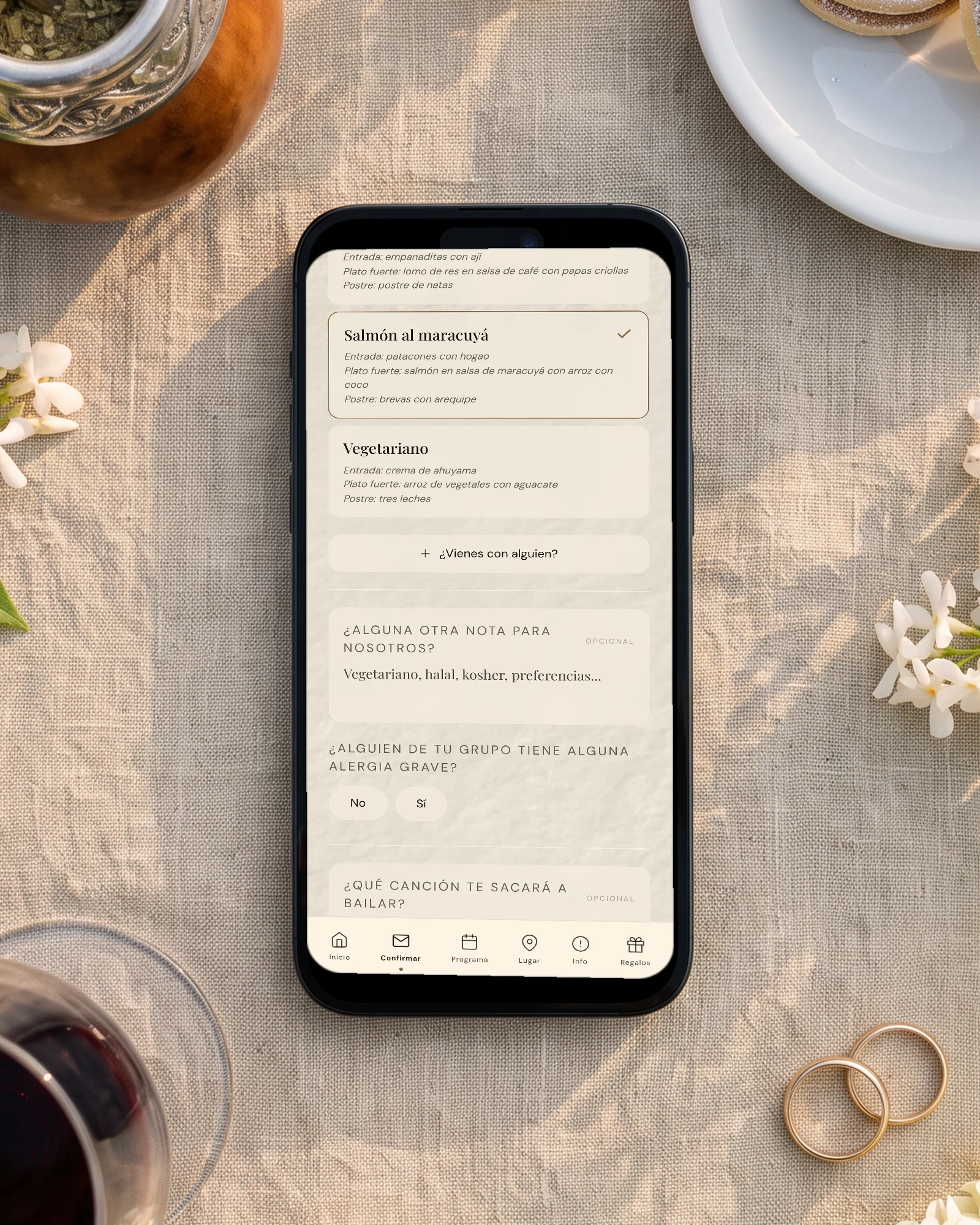 Menú del casamiento en la confirmación: el teléfono muestra la elección de menú con opción vegetariana y la pregunta por alergias graves, entre un mate, alfajores, una copa de Malbec y jazmines