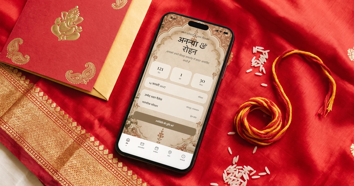 लाल रेशमी दुपट्टे पर रखा फ़ोन जिसमें हिंदी में डिजिटल शादी कार्ड खुला है और नीचे RSVP का बटन है, पास में छपा हुआ लाल-सुनहरा शादी कार्ड, मौली का धागा और चावल के दाने