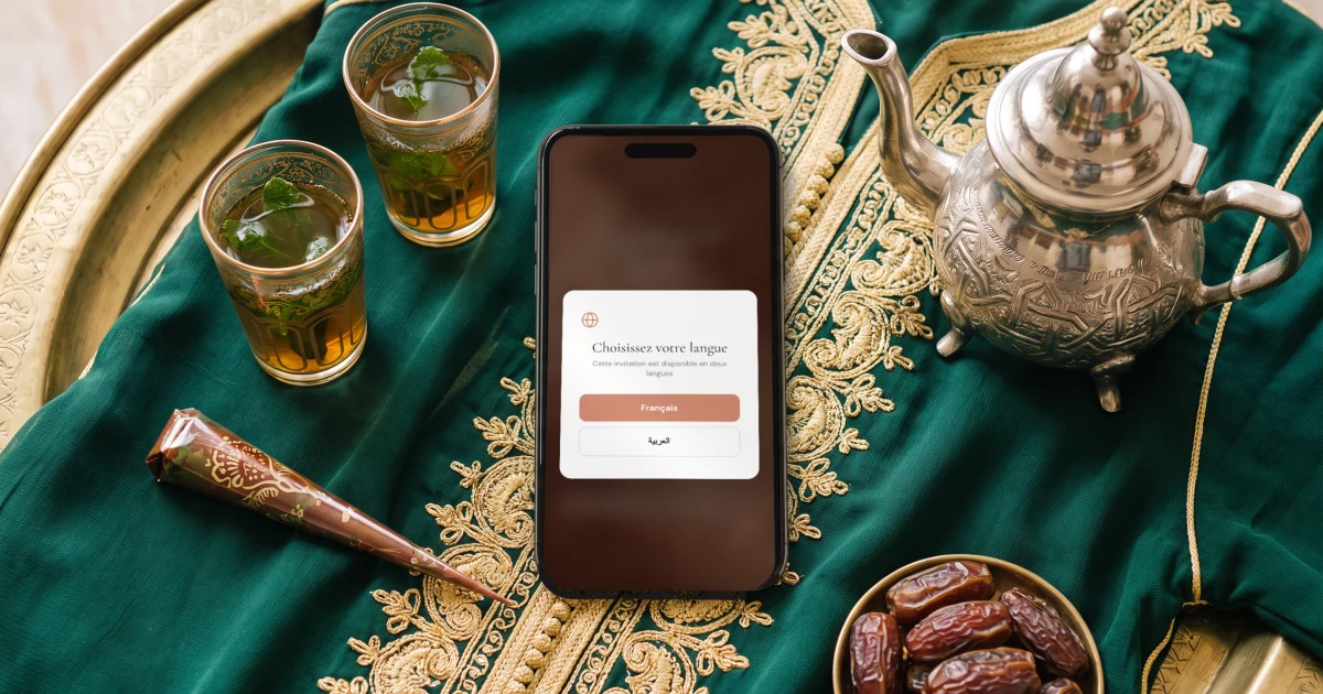 Faire-part de mariage arabe-français : un téléphone affiche le choix de langue du faire-part, français ou arabe, à côté de verres à thé, de henné et d'un caftan brodé