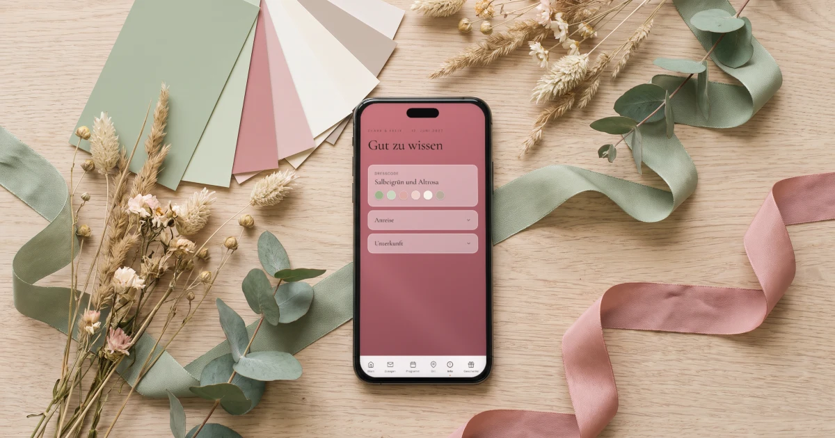 Hochzeitsfarben 2026: ein Handy zeigt die Farbpalette der Einladung neben Farbkarten, Wiesenblumen und Seidenbändern