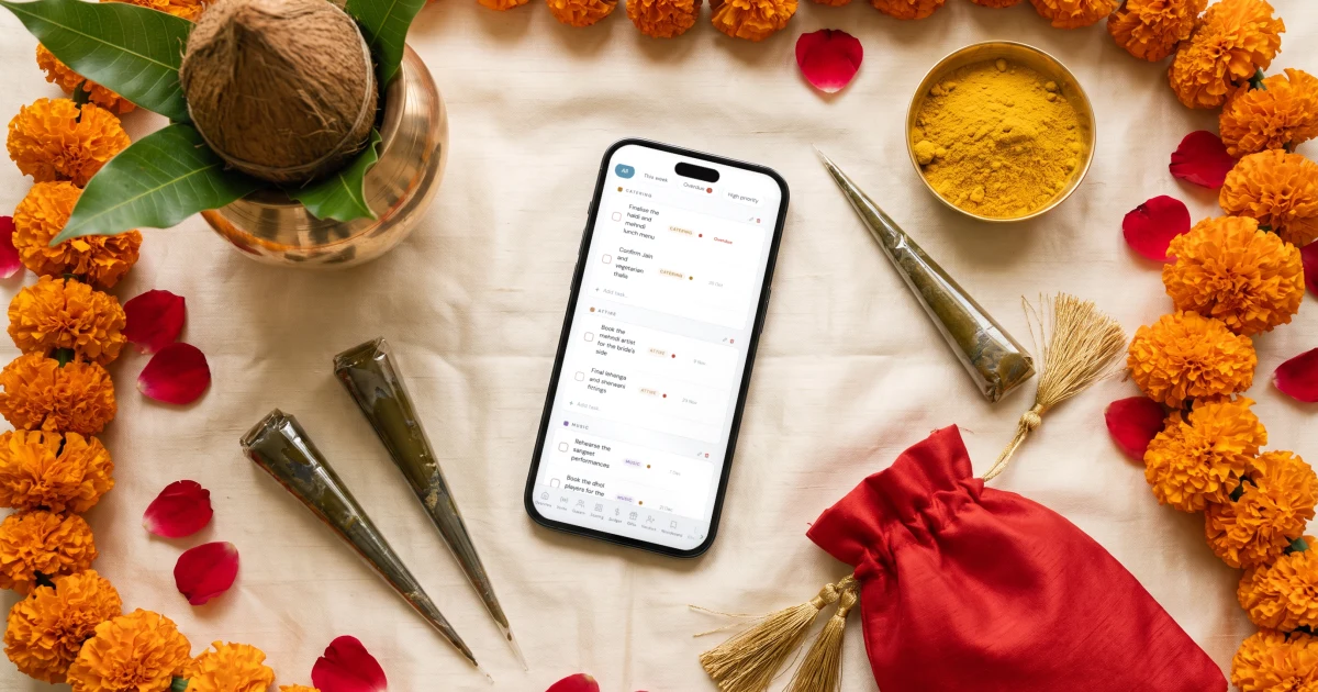 Indian wedding checklist: a phone shows a month by month wedding checklist among marigolds, mehndi cones, a brass kalash and a haldi bowl