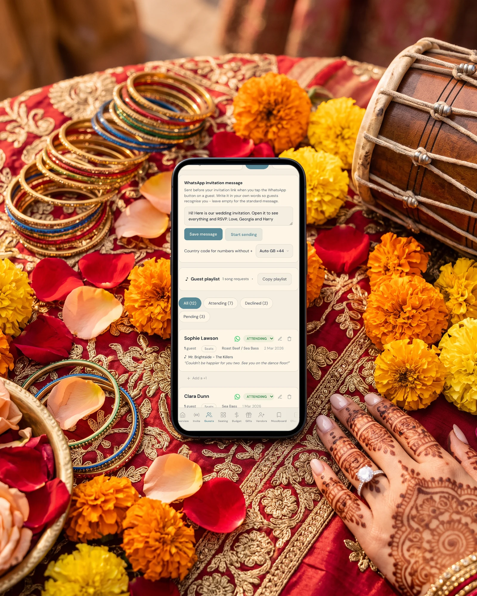 Indian wedding invitations on WhatsApp: a phone shows the WhatsApp invitation message and the guest list with WhatsApp buttons, on red and gold silk with marigolds, bangles, a dholak and a bride's hennaed hand