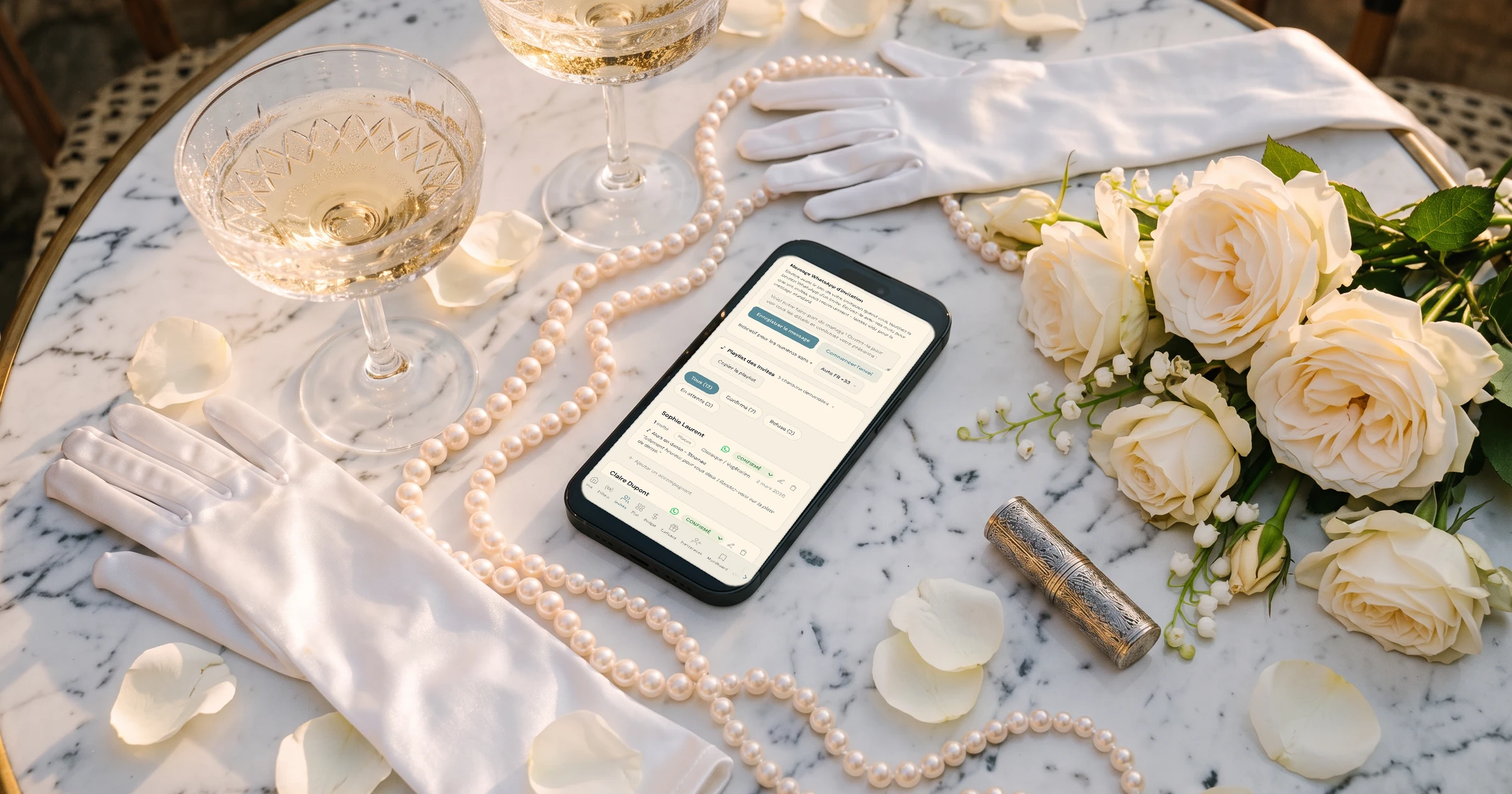 Faire-part vin d'honneur et repas, mariage sur deux jours : un téléphone posé sur une table de marbre parmi des perles, des gants de satin et des roses, dans la lumière dorée, affiche la liste d'invités avec les statuts Confirmé et En attente et le bouton WhatsApp de chaque invité