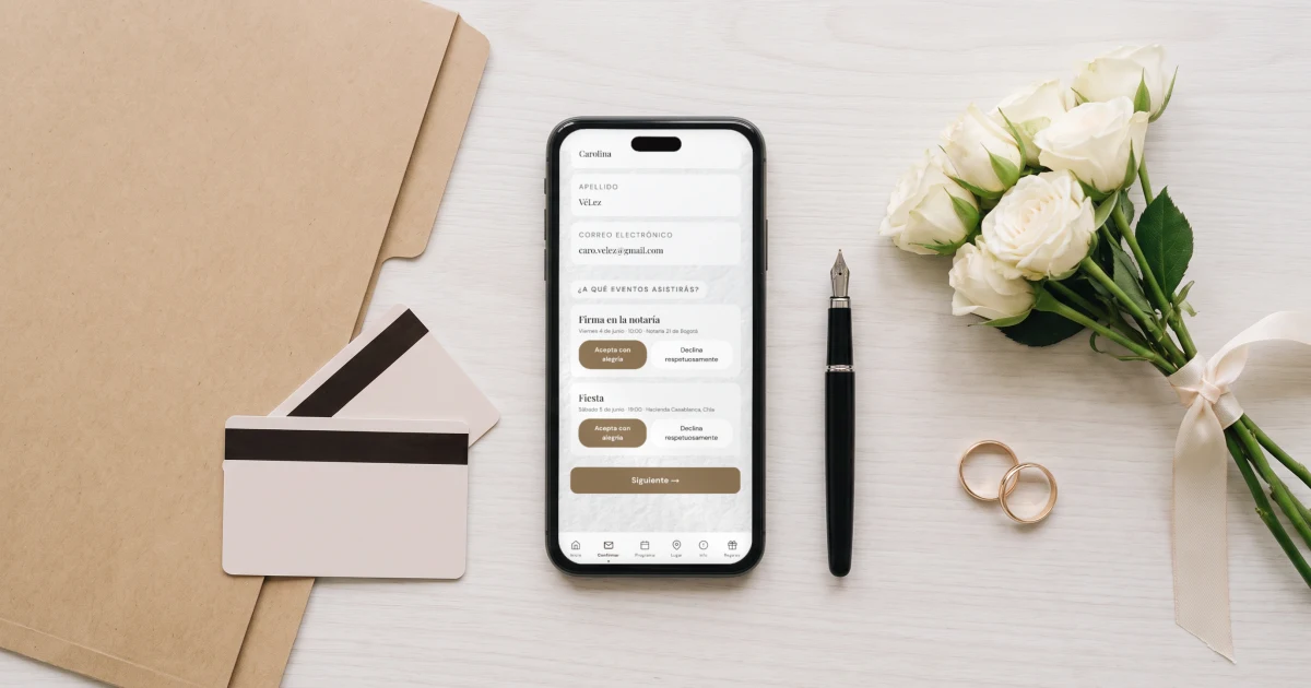 Matrimonio civil en Colombia: un celular sobre un escritorio de madera clara muestra la confirmación de asistencia con dos eventos, la firma en la notaría y la fiesta, junto a una carpeta para el registro civil, dos cédulas boca abajo, una pluma y un ramo de rosas blancas