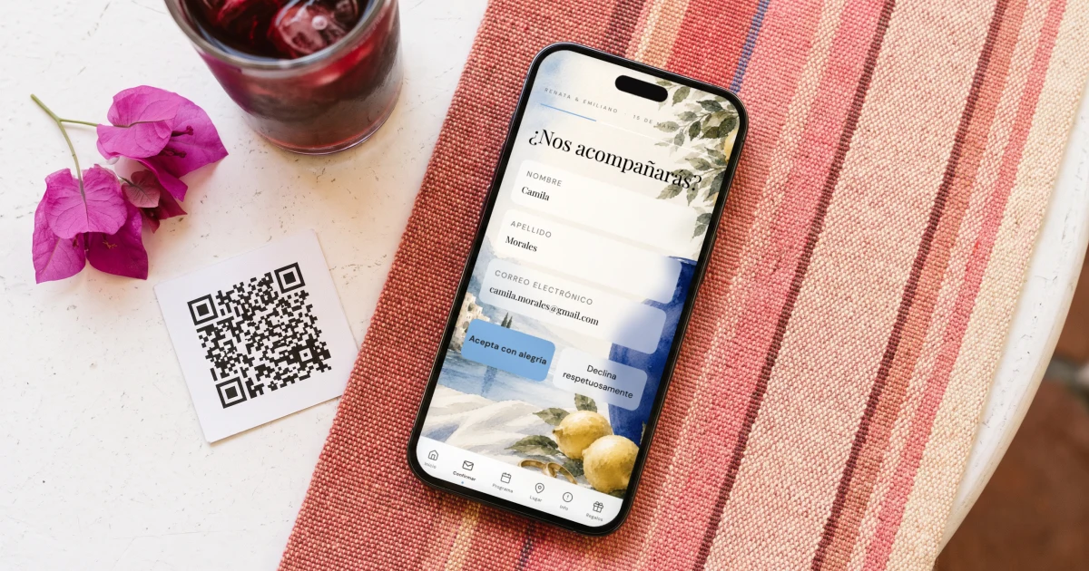 Mejor página web de boda 2026: un teléfono muestra la confirmación de asistencia junto a una tarjeta QR, agua de jamaica y bugambilias