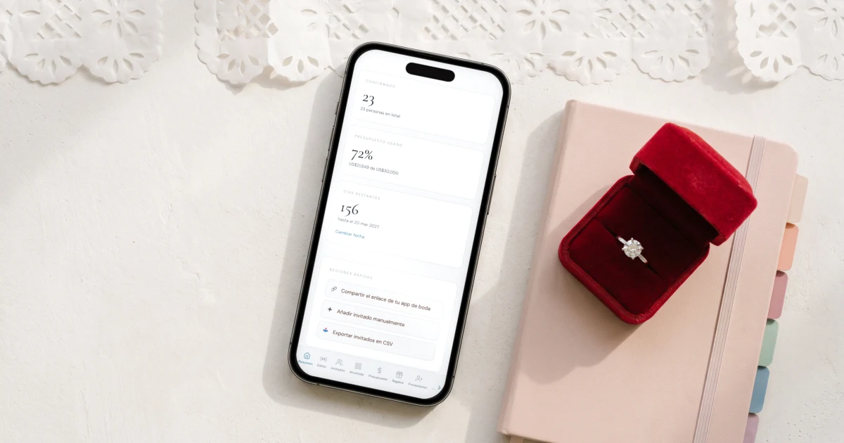 Mejores apps para organizar tu boda: un teléfono muestra el panel de la boda junto a una agenda y una caja de anillos