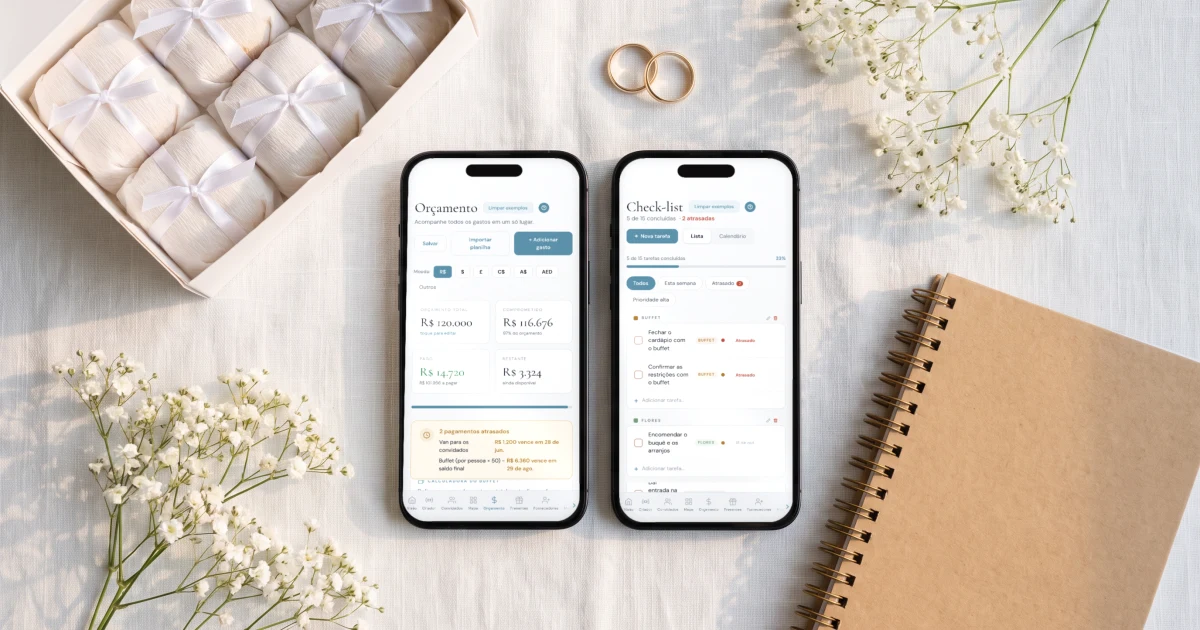 Melhor app para organizar casamento: dois celulares deitados sobre uma toalha de linho branca mostrando o orçamento em reais e o checklist do casamento, ao lado de uma caixa de bem-casados, alianças douradas, um caderno de planejamento e mosquitinho