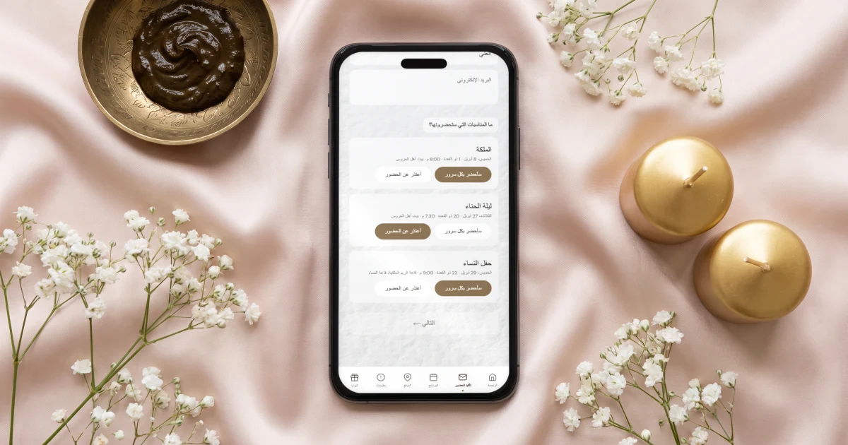 تأكيد الحضور لكل مناسبة في دعوة الزواج: جوال مسطح يعرض نموذج الرد بالعربية لثلاث مناسبات، الملكة وليلة الحناء وحفل النساء، لكل منها سأحضر أو أعتذر، بجانب صحن حناء نحاسي وشموع ذهبية وزهور جبس بيضاء على ساتان وردي فاتح