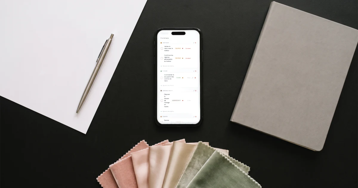 Prix d'un wedding planner : un téléphone affiche la checklist du mariage à côté d'une feuille blanche, d'un stylo et d'un nuancier de tissus