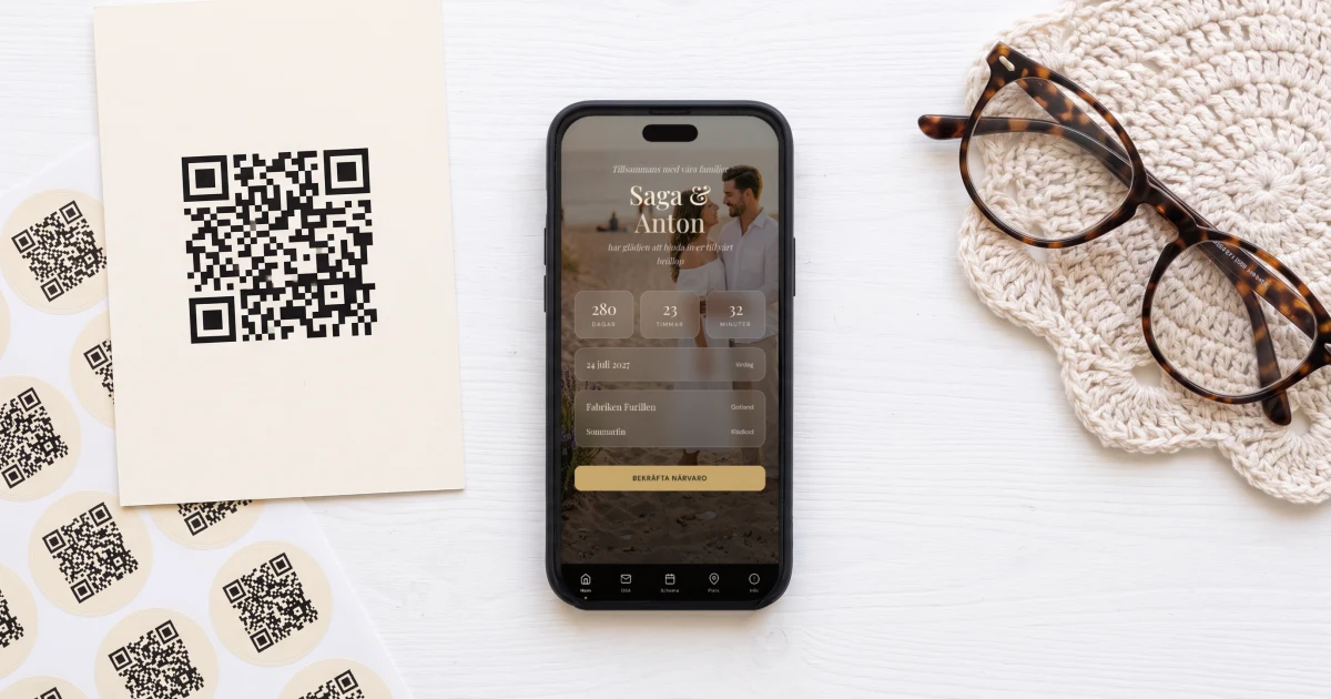 QR-kort till digital bröllopsinbjudan: ett tryckt kort med QR-kod och ett ark med runda QR-klistermärken på ett vitt bord, bredvid en äldre persons läsglasögon och en mobil som ligger platt och visar inbjudans omslag