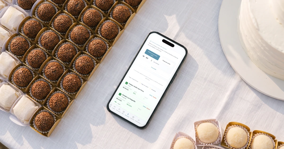 Quanto custa um casamento para 100 pessoas: celular deitado ao lado de uma mesa de doces com bem-casados, brigadeiros e um bolo branco, mostrando a calculadora do buffet com o mesmo preço por pessoa para todos os convidados