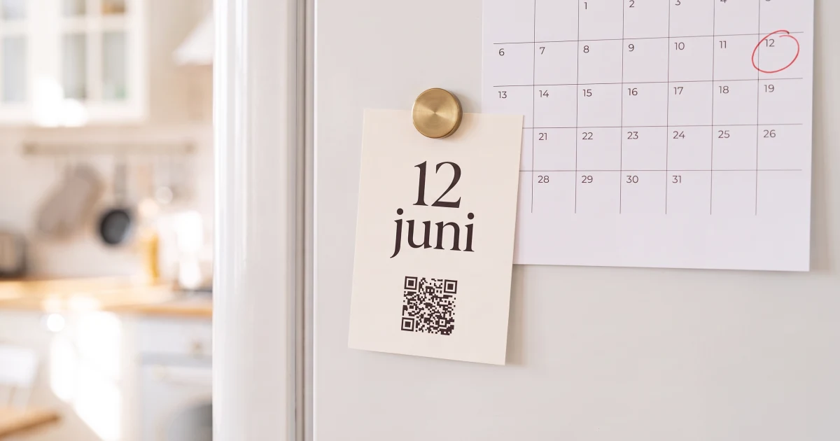 Save the date till bröllop: ett litet kort med datum och QR-kod fäst på kylskåpet med en magnet, bredvid en väggkalender där en lördag i juni är inringad
