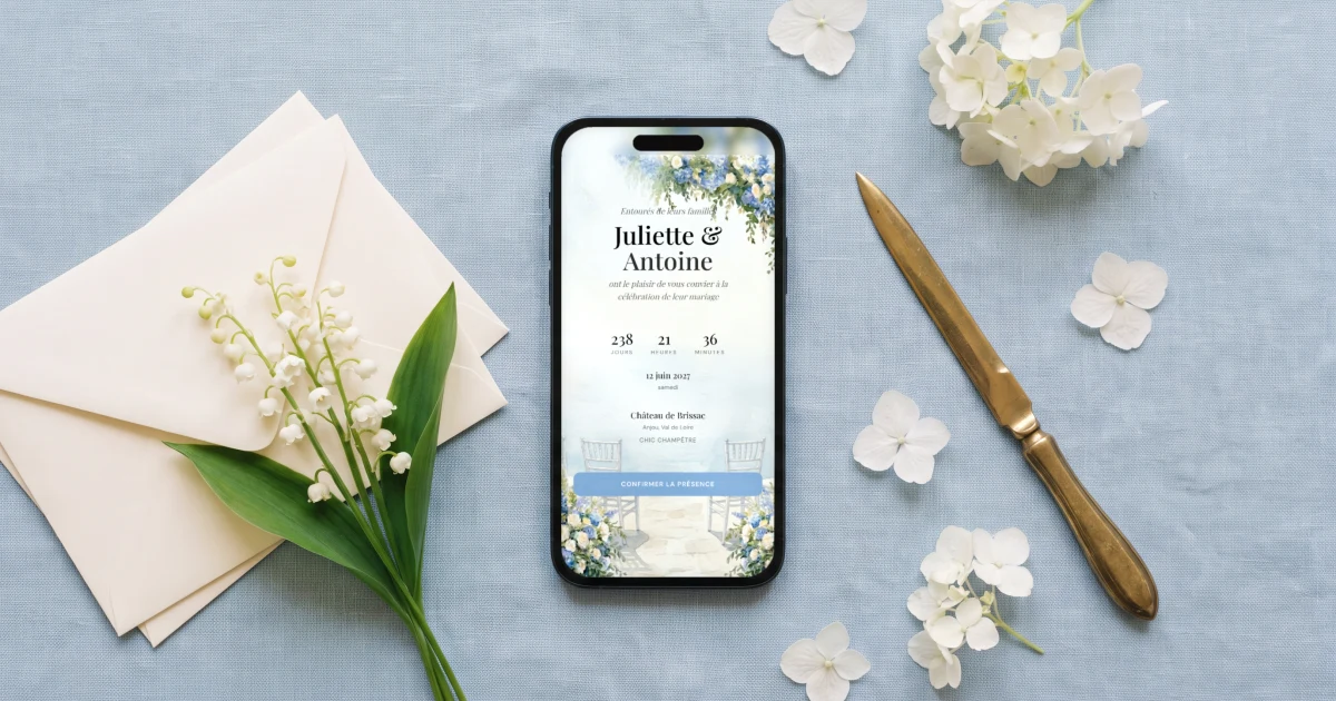 Save the date mariage gratuit ou payant : un téléphone affiche un save the date numérique avec les prénoms, la date et le compte à rebours, à côté d'enveloppes ivoire, d'un brin de muguet et d'un coupe-papier en laiton