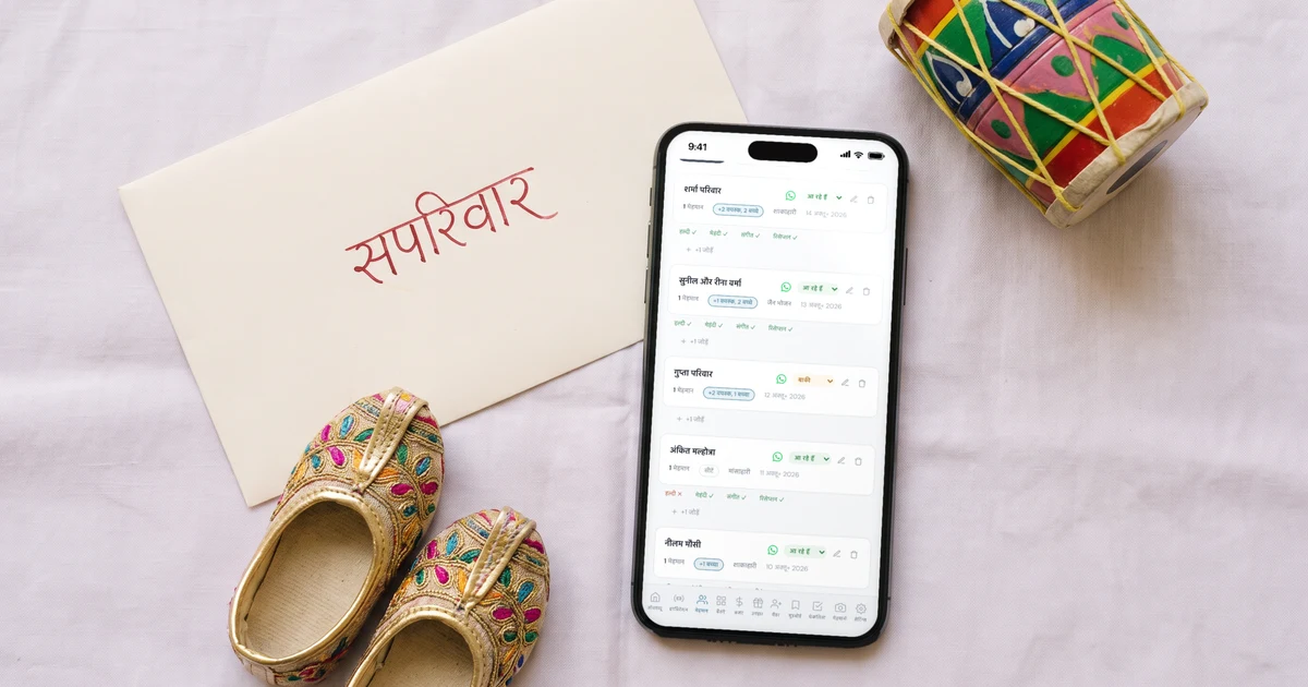 लिफ़ाफ़े पर हिंदी में लिखा “सपरिवार”, पास में बच्चों की छोटी चप्पलें और खिलौना ढोलक, और मेज़ पर रखा फ़ोन जिसमें शादी के इनविटेशन में लिखा है कि इस परिवार के साथ कितने बड़े और कितने बच्चे आ सकते हैं