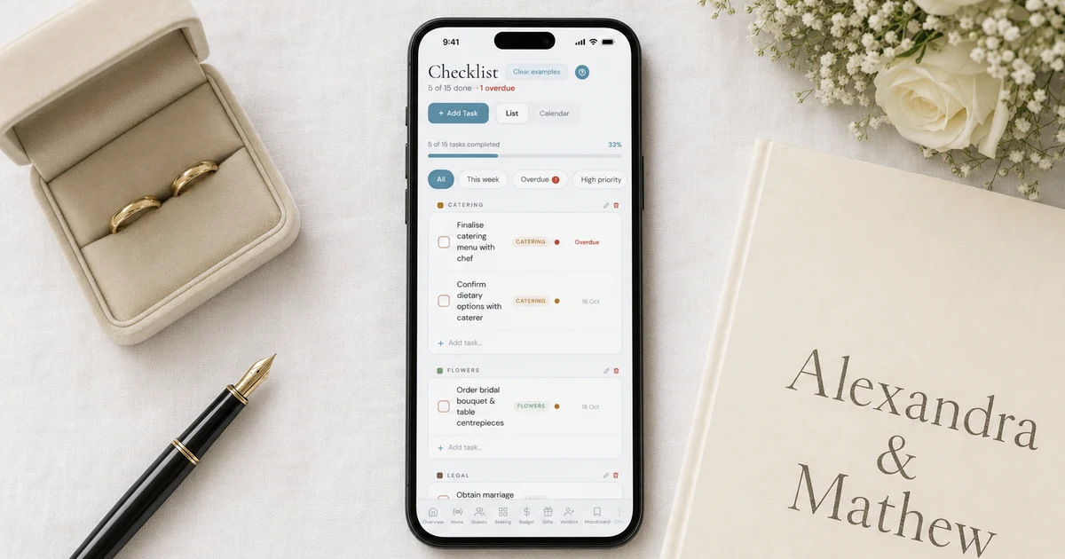 Singapore wedding checklist: a phone showing a wedding planning checklist with tasks, categories and an overdue item, lying on white linen next to wedding rings in a box, a fountain pen, a cream wedding album and white roses