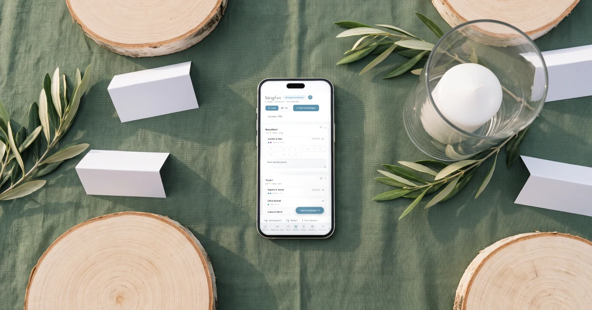 Sitzplan Hochzeit App: ein Handy zeigt den Sitzplan neben Baumscheiben, Tischkarten und einer Kerze