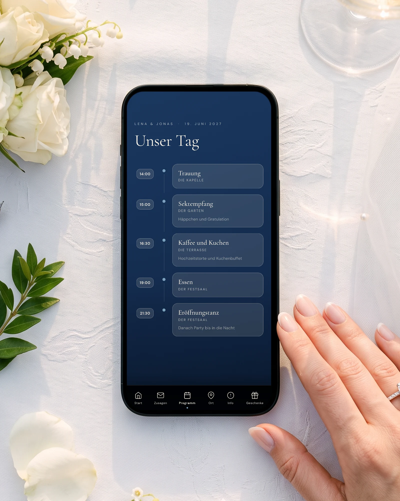 Standesamt, Trauung und Feier: Ein Handy auf weißem Damast neben Brautstrauß, Sektgläsern und Füller zeigt den Ablauf Unser Tag mit Trauung, Sektempfang, Kaffee und Kuchen, Essen und Eröffnungstanz