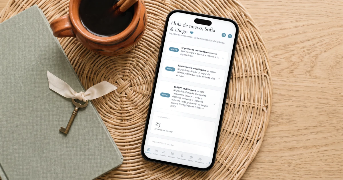 The Private Wedding App sin suscripción: un teléfono muestra el panel de la boda junto a una agenda, una llave de latón y un café de olla