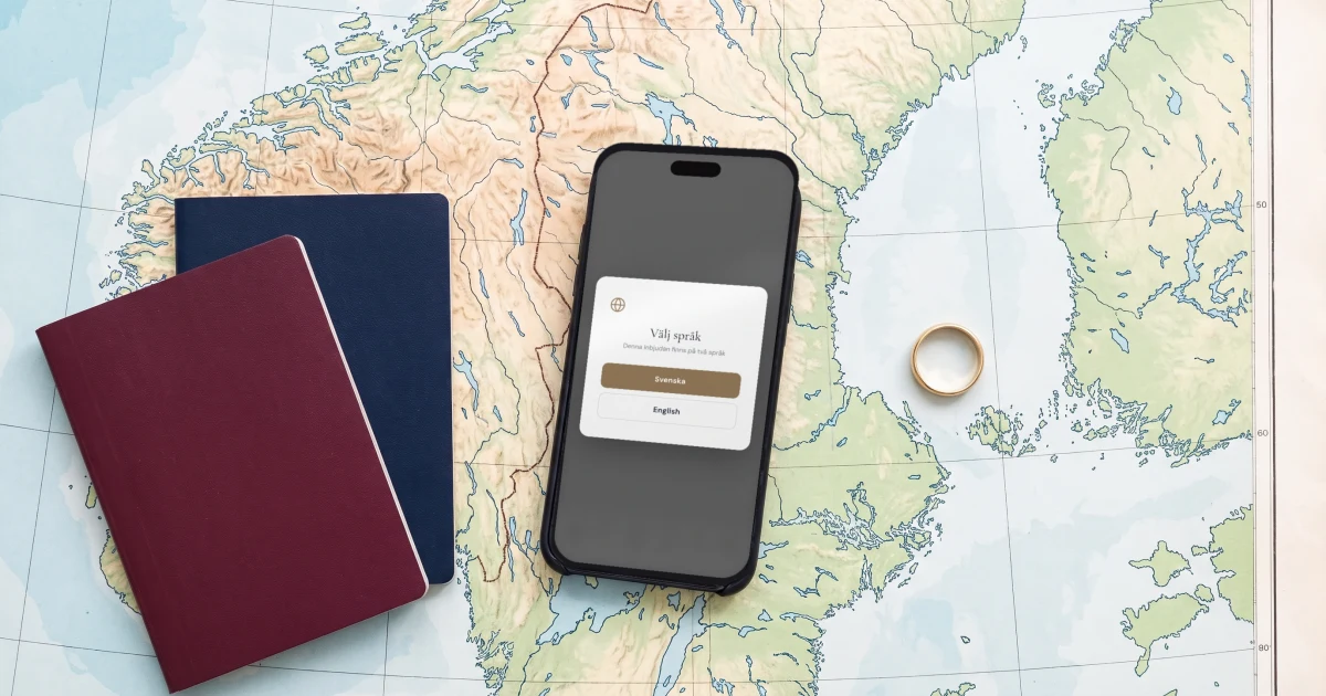 Tvåspråkig bröllopsinbjudan på svenska och engelska: mobilen visar språkvalet i inbjudan, liggande på en karta över Sverige bredvid två pass och en vigselring