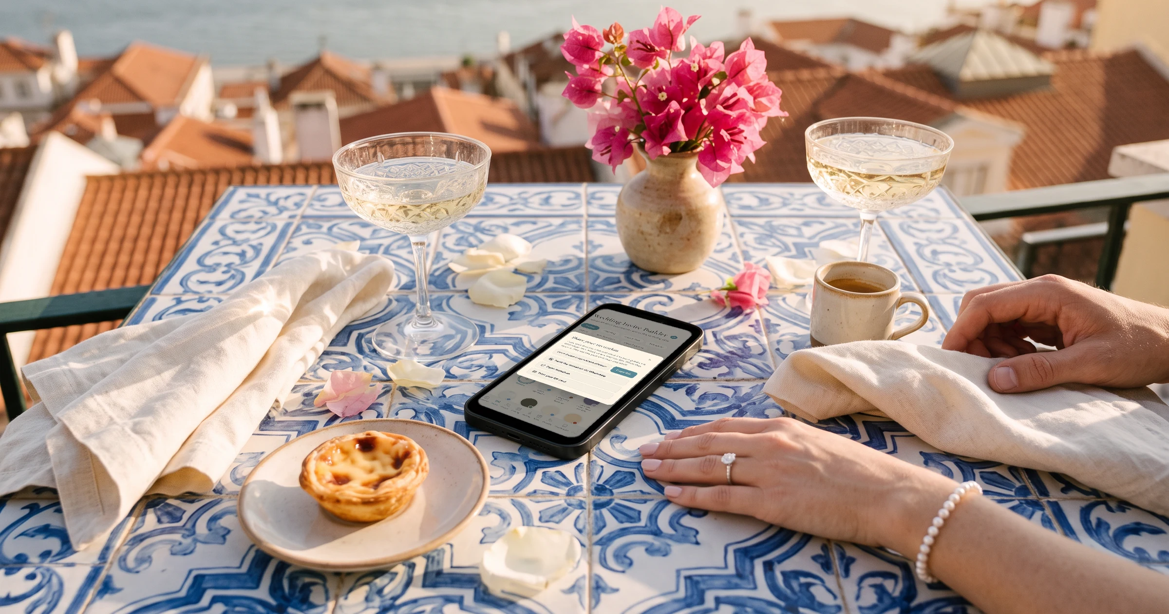 Wedding invitation share panel on a phone with Send the invitation via WhatsApp, on a Lisbon balcony table of blue and white azulejo tiles with a pastel de nata, bougainvillea and a bride's hand