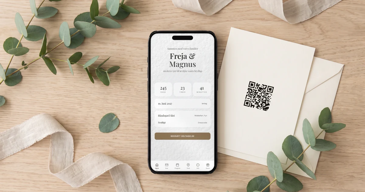 Bryllupshjemmeside med tilmelding: et trykt invitationskort med QR-kode ligger ved siden af en telefon, der viser bryllupshjemmesidens forside med brudeparrets navne, dato og program, på et lyst egetræsbord med eukalyptus