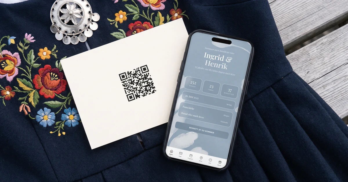 Trykt bryllupsinvitasjon med QR-kode som ligger på et bunadsforkle med sølvsølje, ved siden av en mobiltelefon flatt på bordet som viser forsiden av bryllupsnettsiden med navnene og nedtellingen