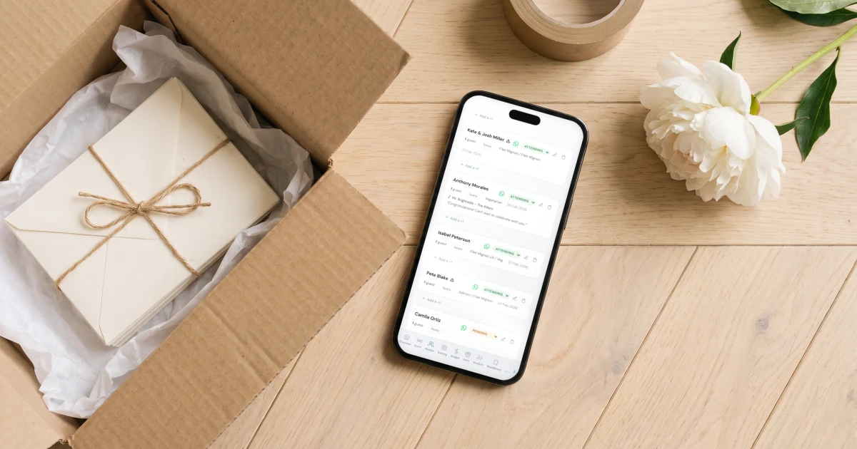 Zola alternatives 2026: a phone shows a wedding guest list with RSVPs and meal choices, next to a moving box with wedding stationery being packed