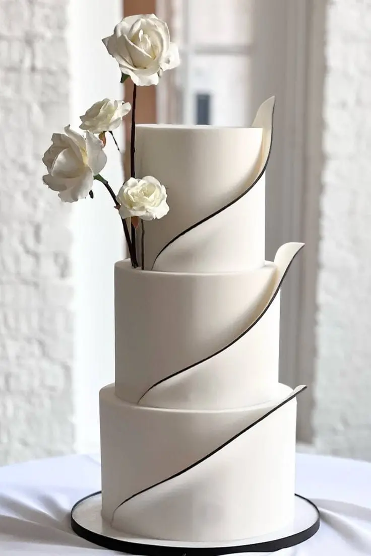 Modern three-tier white wedding cake with sculptural fondant and white roses