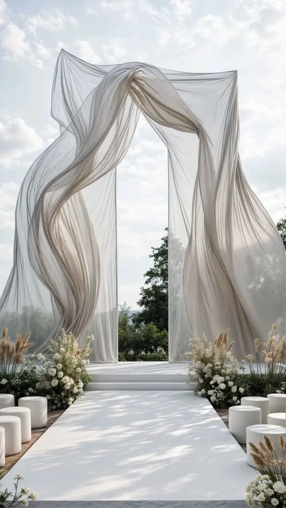 Outdoor wedding ceremony arch with flowing draped fabric and white flowers